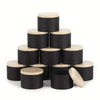 A set of black metal candle tins with natural wood lids stacked in a pyramid formation.