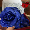 A close-up of a vibrant blue glitter artificial rose flower being held, set against a red box.