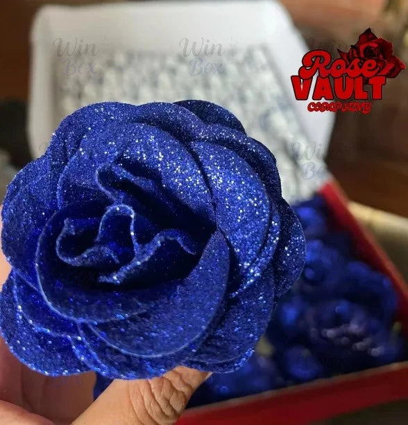 A close-up of a vibrant blue glitter artificial rose flower being held, set against a red box.