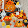 A festive display of artificial orange and yellow carnation and marigold flower heads arranged around pumpkins and seasonal f