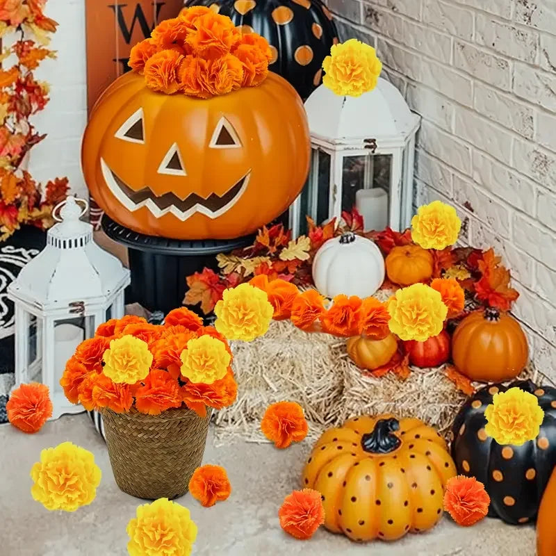 A festive display of artificial orange and yellow carnation and marigold flower heads arranged around pumpkins and seasonal f