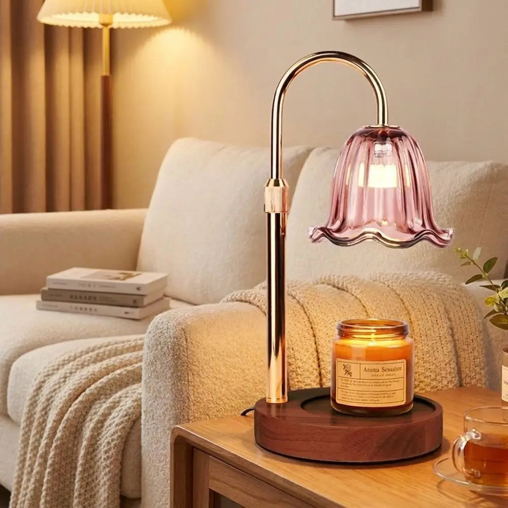 A modern gold-toned adjustable aromatherapy candle warmer lamp with a pink glass shade on a wooden table.