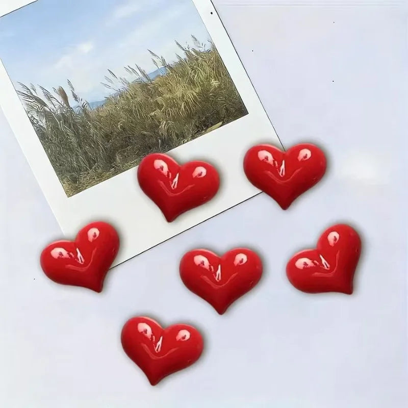 A set of red heart-shaped fridge magnets placed on a white surface next to a photo.