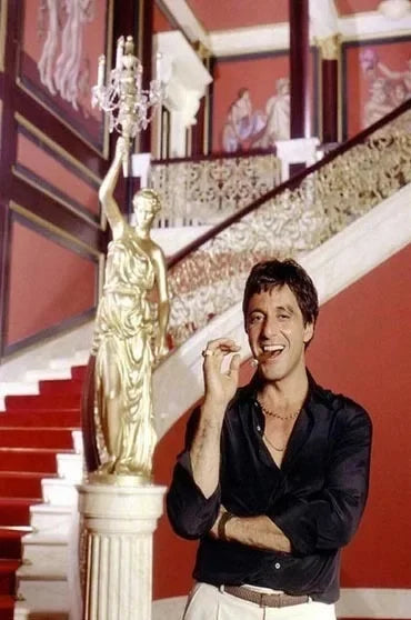 Un homme en chemise noire et pantalon blanc se tient à côté d'une statue dorée sur un escalier.