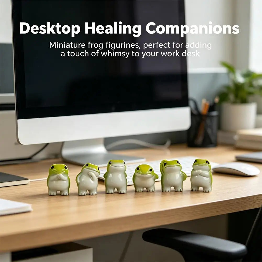 A set of six cute mini resin frog figurines placed on a wooden desk next to a computer monitor.