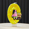 A yellow sponge cake candle shaped like the number 0, decorated with characters from SpongeBob SquarePants.