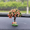A miniature tree ornament featuring pink and white flowers displayed on a black car dashboard.