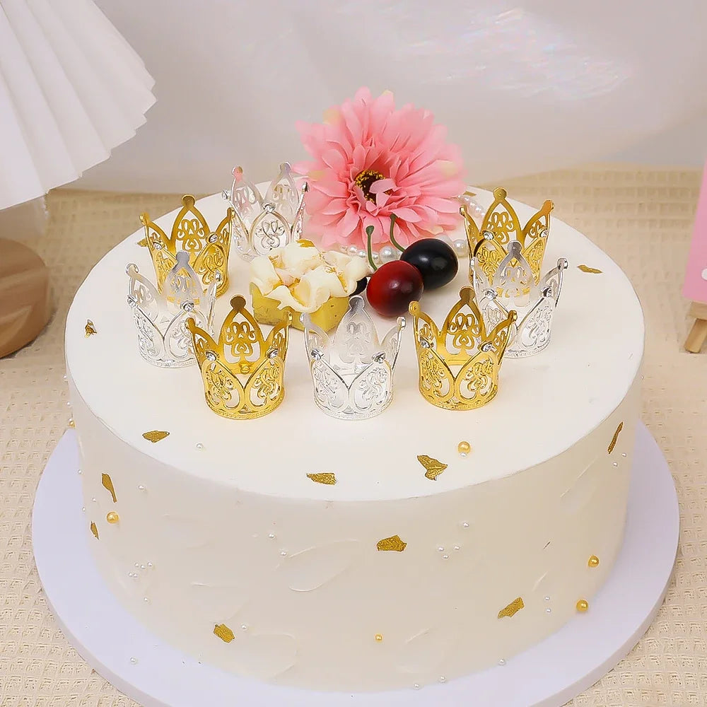 A white cake decorated with gold crown toppers, pink flowers, and dark berries for a celebration.