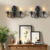 Vintage black wall pendant candle holder with multiple taper candles mounted on a light beige wall.