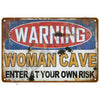 A vintage metal tin sign with a warning label that reads WARNING WOMAN CAVE ENTER AT YOUR OWN RISK