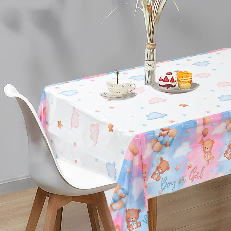 A white tablecloth decorated with pink and blue clouds, bears, and stars for a gender reveal party.