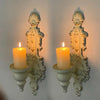 A pair of vintage wrought iron wall-mounted candle holders with glowing white candles.
