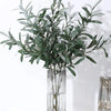 Artificial olive branch with green leaves and small fruits displayed in a clear glass vase.
