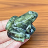 Une petite figurine de grenouille de jade miniature est tenue dans une main sur un fond en bois.