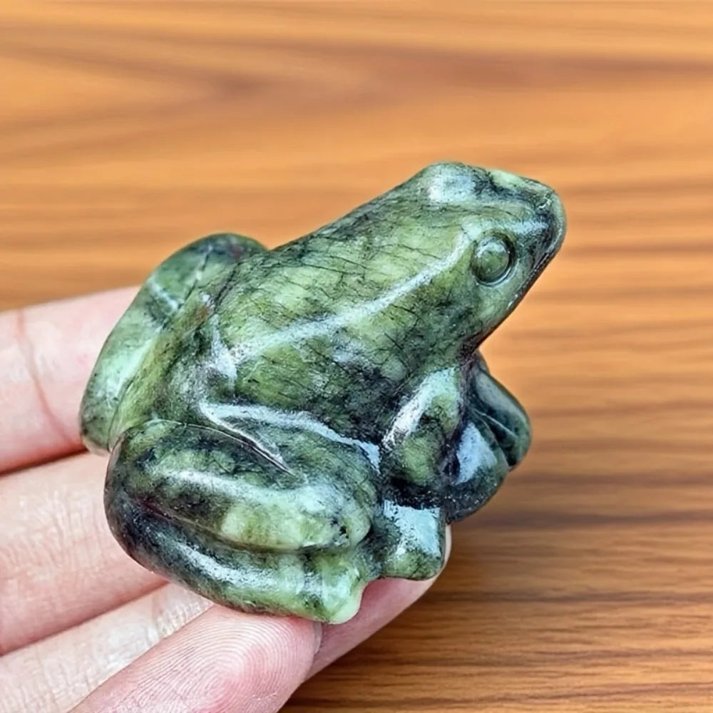 Une petite figurine de grenouille de jade miniature est tenue dans une main sur un fond en bois.