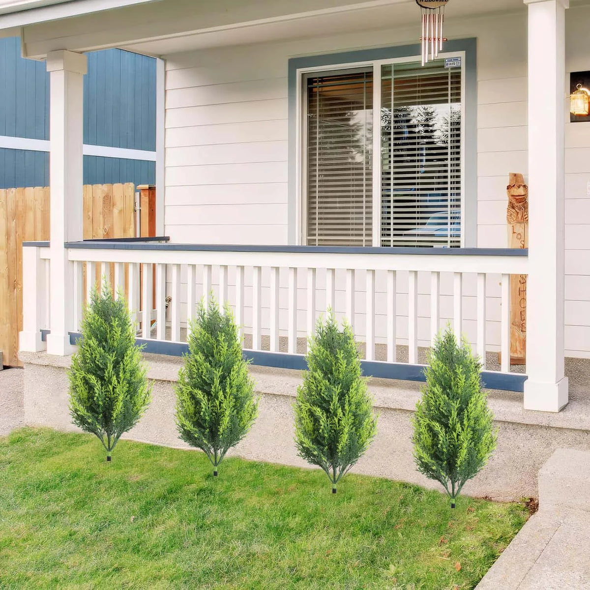 Two artificial green fern stakes are planted in a lawn next to a white porch railing and siding.