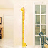 A yellow giraffe-shaped height chart wall sticker with markings, displayed on a white wall next to a window.
