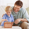 A man is helping a child place coins into a wooden money saving box with a built-in goal tracker.