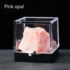 Pink opal rough stone specimen displayed in a clear box on a dark surface.