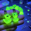 A hand holds glow-in-the-dark resin charms shaped like an alien cat and a duck against a dark blue background.