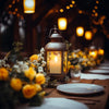 A close-up of a glowing LED tea light in a metal lantern set on a wooden table with floral arrangements and warm bokeh lights
