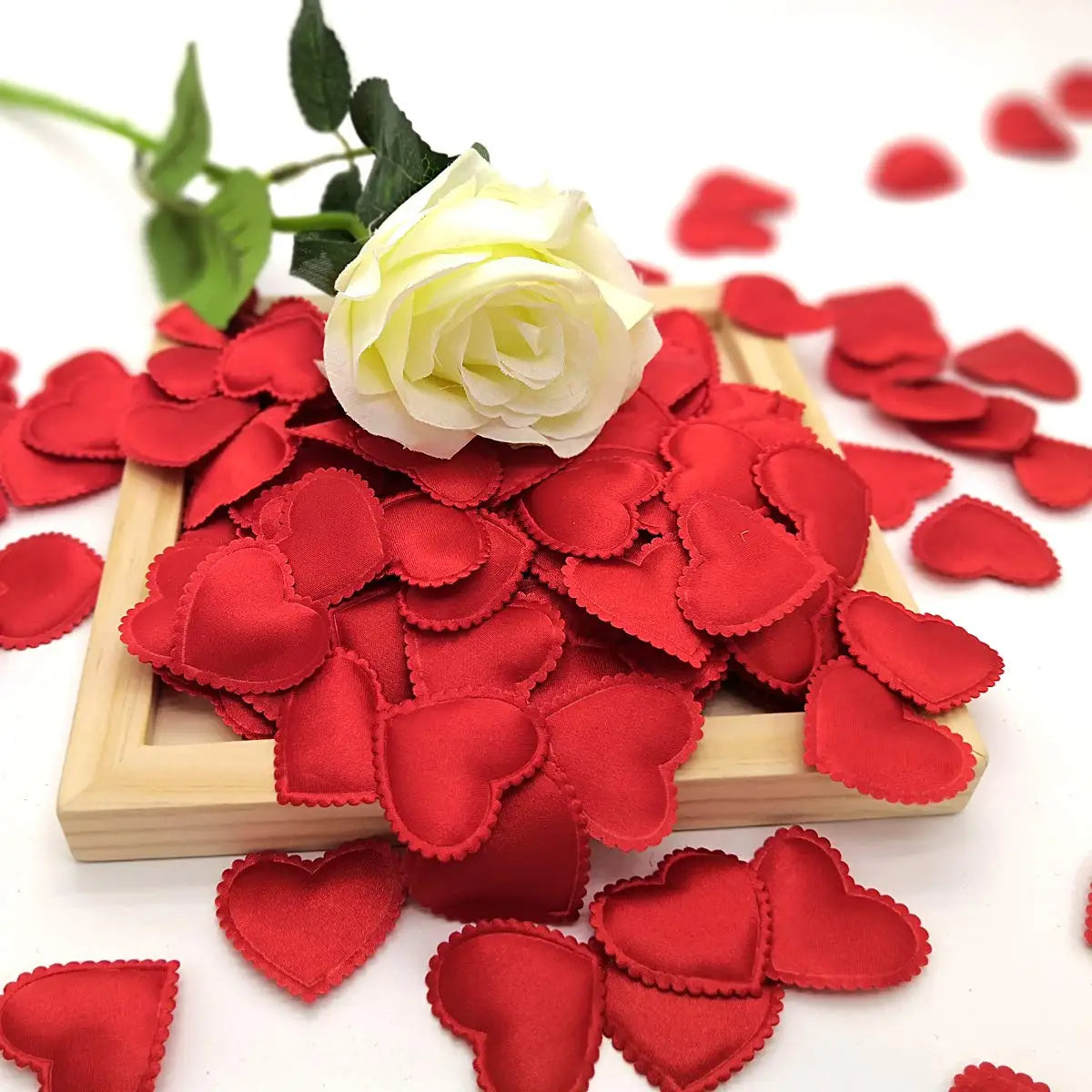 A pile of red fabric heart petals is displayed in a wooden tray on a white background.