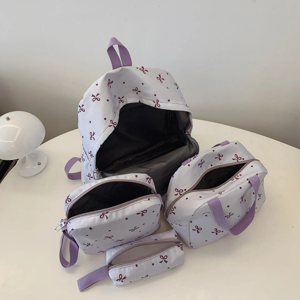 A set of women's backpacks and accessories featuring a white background with small purple bow prints.