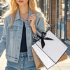 A blonde woman wearing a denim jacket holds an elegant black and white gift bag with a black bow ribbon.