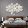 A bedroom wall decorated with a cluster of 12 self-adhesive hexagon mirror stickers on a gray wall above a wooden bed.