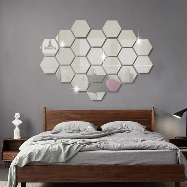A bedroom wall decorated with a cluster of 12 self-adhesive hexagon mirror stickers on a gray wall above a wooden bed.