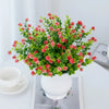 A bouquet of artificial eucalyptus branches with red flowers in a white vase on a white table.