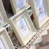A wooden photo frame with a floral design is displayed on a lace tablecloth.