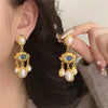 Gold and blue eye pearl drop earrings with dangling charms displayed against dark hair