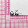 Two small black and white resin penguin figurines are measured against a pink ruler.
