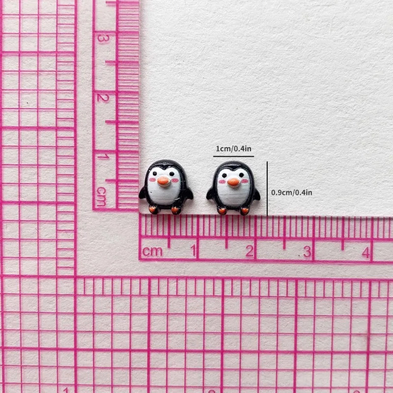 Two small black and white resin penguin figurines are measured against a pink ruler.