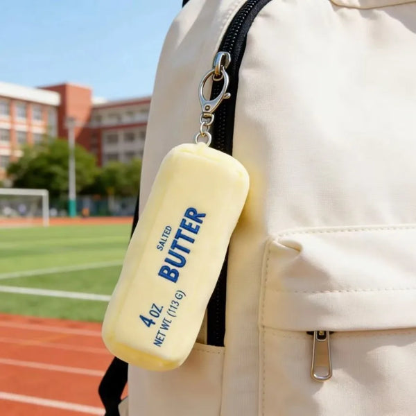 A yellow salted butter squishy keychain attached to a beige backpack zipper pull.
