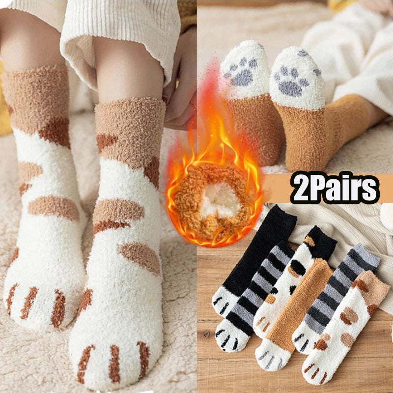 A pair of beige and white plush socks featuring cat paw prints, displayed next to a glowing fire.