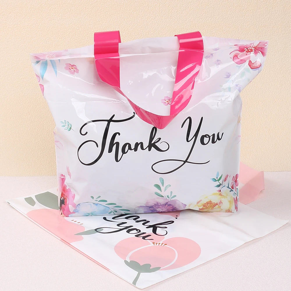 A white floral thank you gift bag with pink handles and black script writing on the front