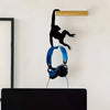 A black monkey-shaped storage hook with a banana design is mounted on a light wood shelf above a black desk.