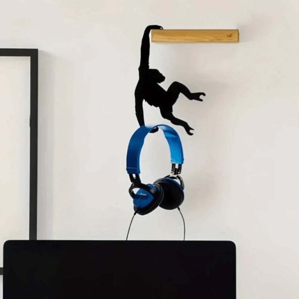 A black monkey-shaped storage hook with a banana design is mounted on a light wood shelf above a black desk.