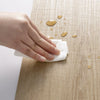 A hand wipes a wood grain peel-and-stick sticker on a wooden surface, with loose stickers scattered nearby.
