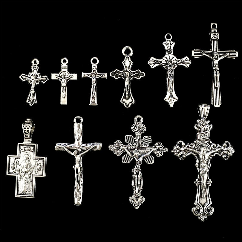 A collection of antique silver cross charms and pendants for jewelry making displayed against a black background.
