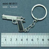 A silver miniature replica of a pistol is attached to a keyring, measured against a millimeter ruler.
