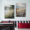 A framed oil painting depicting a serene river landscape with fields of white daisies.