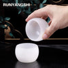 A hand holds a smooth, white crystal agate healing bowl for home decor against a dark background.