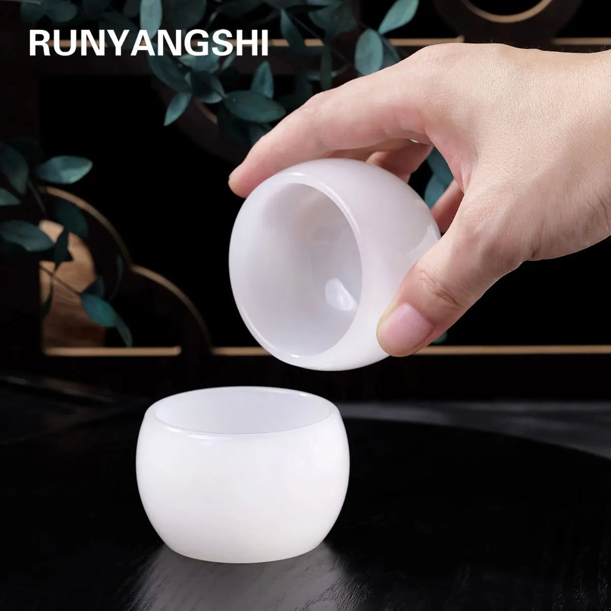 A hand holds a smooth, white crystal agate healing bowl for home decor against a dark background.