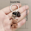 A small brown teddy bear charm attached to a silver keyring and a coffee-themed pendant.