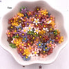 A collection of colorful 3D resin flower gems in various shades of pink, yellow, purple, and brown arranged in a white dish.