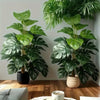 Two large artificial monstera palm plants with lush green leaves displayed on a wooden surface.