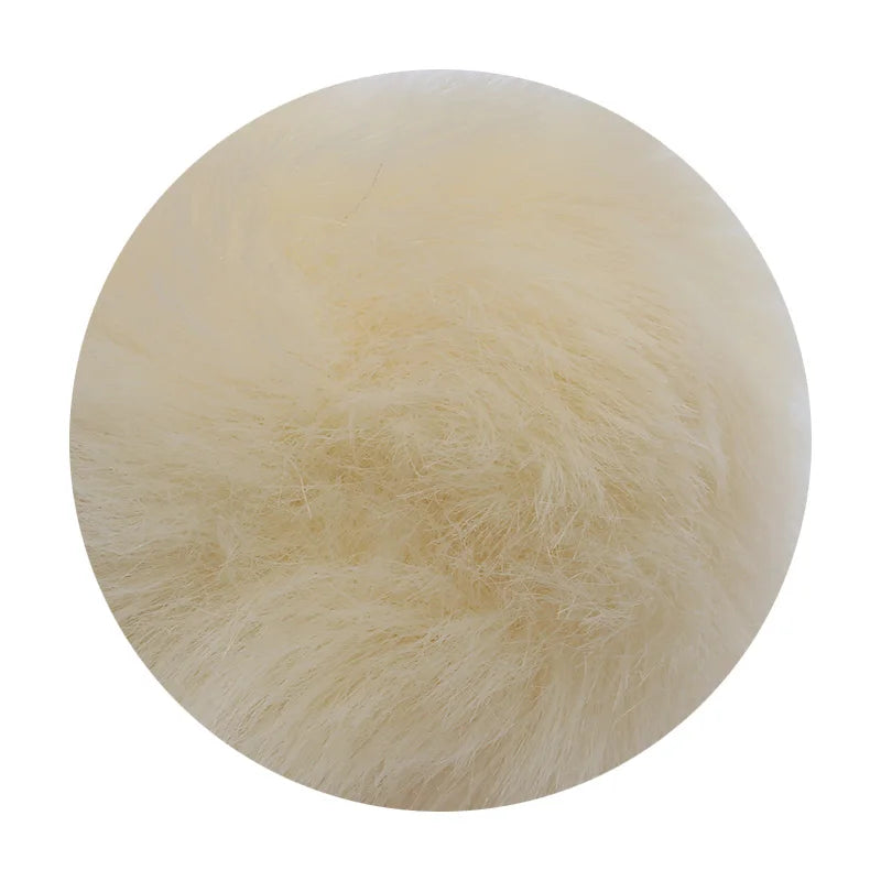 A round pom pom made of light beige faux fur with a silver chain attached.